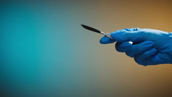 Doctor Hand in Protective Glove Holding Scalpel on Blurred Background