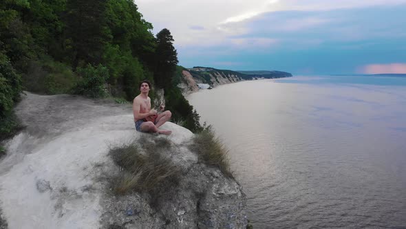 Young Shirtless Man Playing Ukulele on the Cliff Around the Forest and River in Early Morning