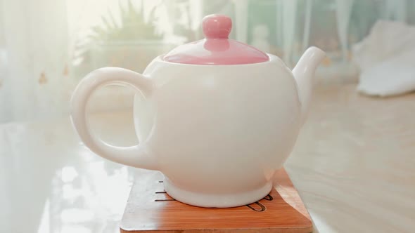 Close-up of a white porcelain teapot standing on a stand on the table. Zoom in. Tea time concept.