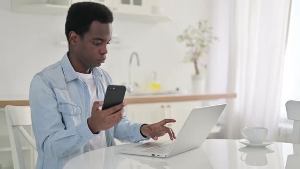 African Man Working on Smartphone and Laptop at Home