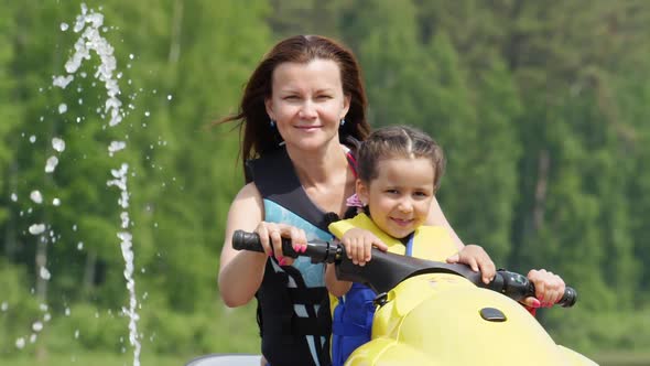 Mom and Daughter Ride Along the River on a Personal Watercraft
