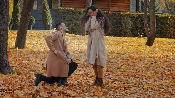 Hispanic Loving Couple in Autumn Park Man Stand in Yellow Leaves on One Knee Making Marriage