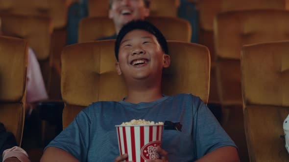 Handsome cheerful young asian boy laughing while watching film in movie theater.
