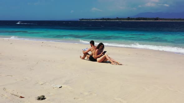 Teenage lovers tanning on marine coast beach break by aqua blue ocean and white sandy background of 