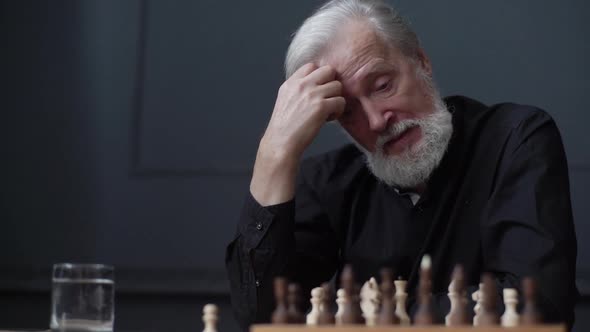 Closeup of Grayhaired Mature Adult Male Thinking About Chess Move Sitting at Home and Playing Chess