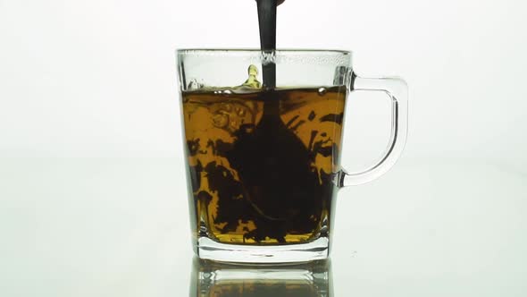 Spoon Stirs Tea in Transparent Glass Cup Creating Whirl, Black Particles Spinning Brewing Tea. Slow
