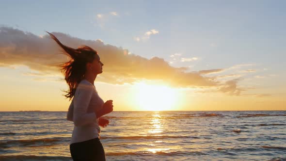 Young Attractive Woman Jogging on the Beach at Sunset. Beautiful Clouds and Breathtaking Sunset