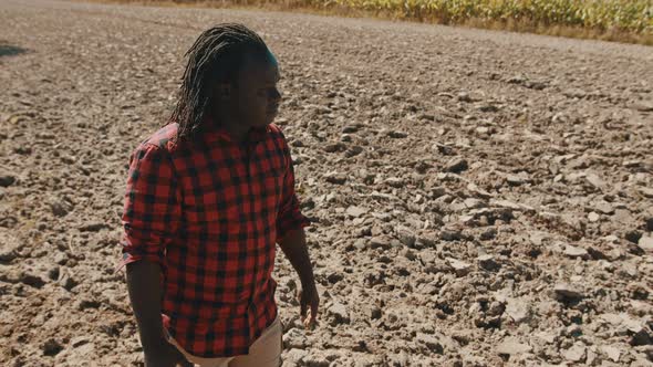 Portrait of Young African Farmer Standing on the Agricultural Plowed Land and Looking Around