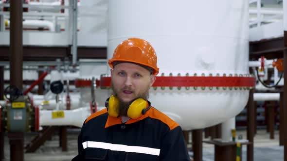 Portrait of an Employee in a Work Helmet and Headphones in Overalls