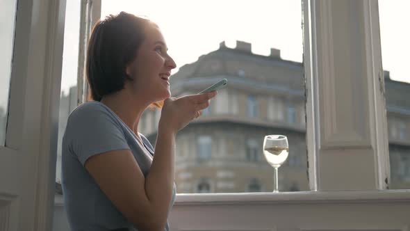 Side View of a Young Woman Using the Voice Recognition of the Phone While Drinking Wine and Sitting