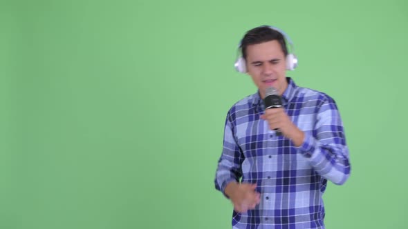 Happy Young Handsome Hipster Man Listening To Music and Singing with Microphone