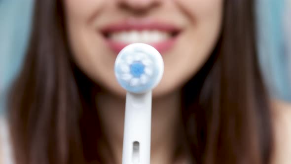 smiling young woman holding electric toothbrush, turning on, rotative moves. dental care concept. or