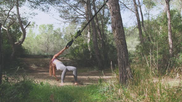 Full length of active woman doing suspension training barefoot in forest