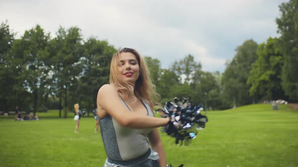 Portrait of Happy Cheerleader Woman Dancing with Pom-poms in Park