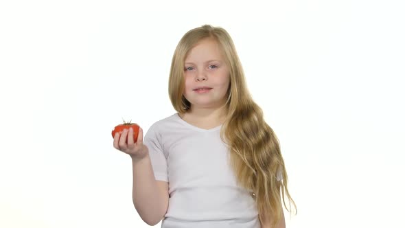 Child Looks at a Tomato, Admires It and Smiles. White Background