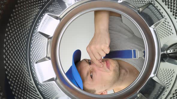 Master repairman looks inside washing machine, smells stench and plugs his nose