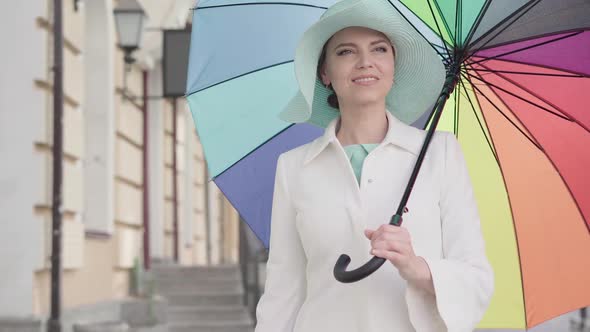 Camera Approaches To Elegant Adult Caucasian Woman Standing Outdoors with Colorful Umbrella and