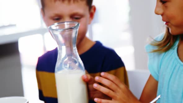Girl pouring milk into cereal bowl in kitchen alt