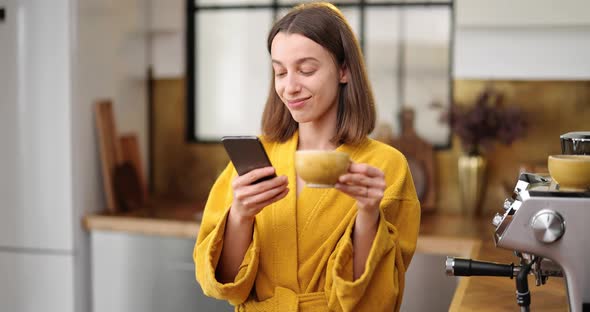 Woman with Coffee and Phone on the Kitchen in the Morning