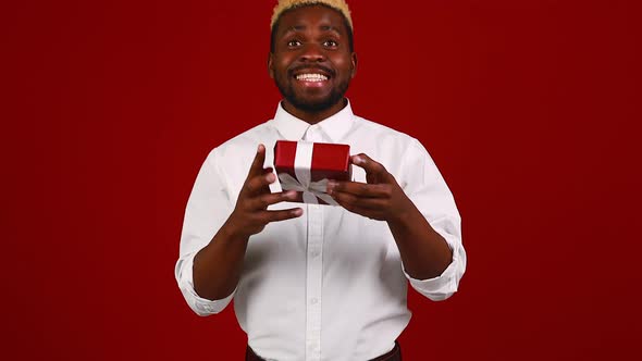 Latin Hispanic Man in White Tshirt in Red Studio Background with Small Gifts Box