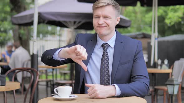 Thumbs Down by Businessman Sitting in Outdoor Cafe