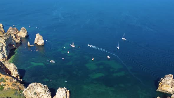 Drone shot of kayaks and boats passing in the ocean, people exploring caves and tunnels.