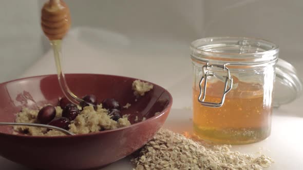 Drizzling golden runny honey over porridge and cranberry breakfast