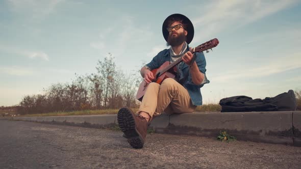 Young Man Playing Guitar and Sitting on Ground in Urban Road