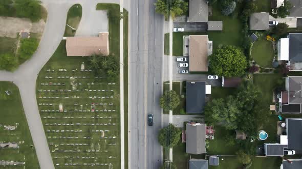 Aerial top down of car on road surrounded by housing area and cemetery in Welland