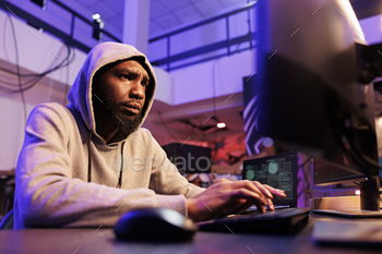 nto computer network system. Concentrated african american man in hood engaging in online criminal activity and breaking law