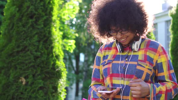 Cheerful African American Woman with an Afro Hairstyle with Packages After Shopping Uses a