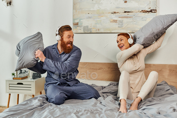 dhead husband and wife, happy couple in wireless headphones pillow fight, bearded man and carefree woman, tattooed music lovers, weekends