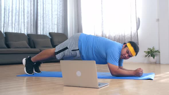 Overweight Man Struggling To Do Plank Exercising At Home While Looking At His Laptop