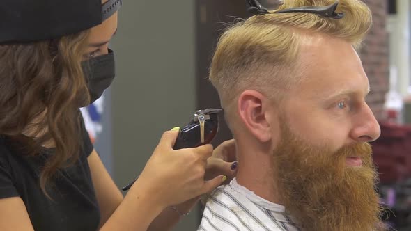 Close up of professional young barber girl in mask doing haircut for her client.