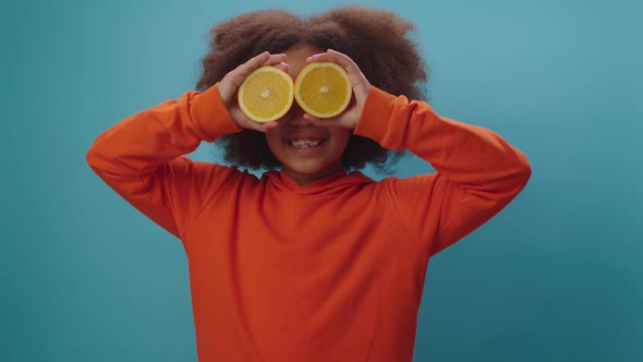 Happy African American girl holding two orange fruit halves hear face