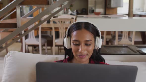 Mixed race woman on couch at home using laptop listening to music