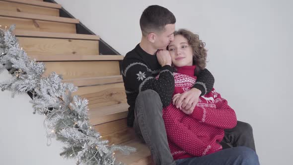 Portrait of Young Romantic Couple Sitting on Stairs at Home on Christmas Eve. Happy Handsome Man