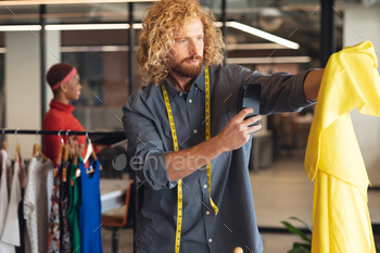 Young caucasian male fashion designer photographing fabric with smart phone in office
