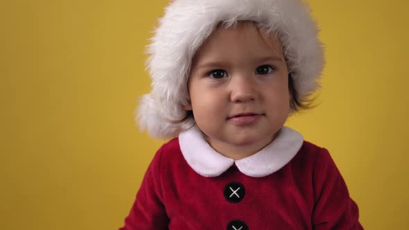 Close Up Emotion Cute Happy Cheerful Chubby Toddler Baby Girl in Santa Suit Looking On Camera At