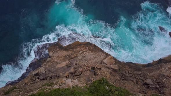 Ocean waves crashing and hitting against cliff and rocks bird eye view aerial drone shot.