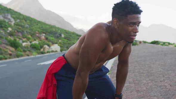 African american man exercising outdoors leaning on his knees on a coastal road