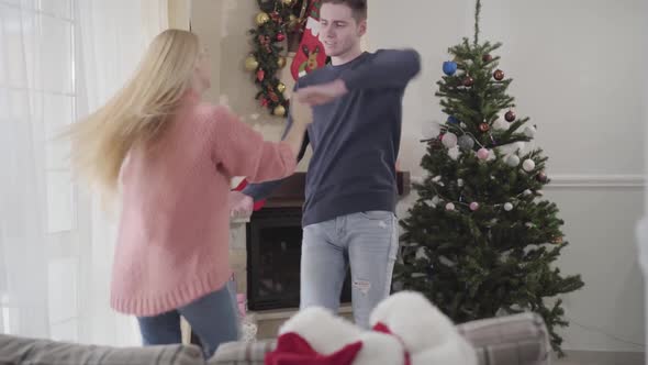 Young Caucasian Man and Woman Dancing in Front of Christmas Tree at Home. Positive Couple Spending
