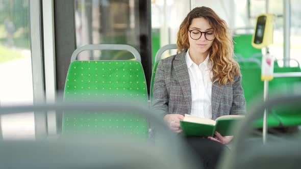 Caucasian young woman rides public transport, sits on a seat reading a book by the bus window