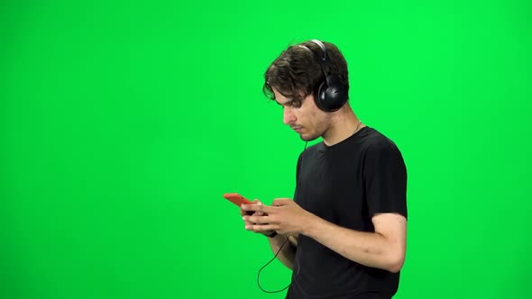 Man in Big Headphones Goes and Texting with Smartphone on Green Screen at Studio. Slow Motion