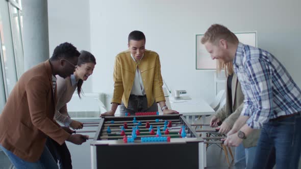 Young handsome casual multiethnic business people playing table football and relaxing at office