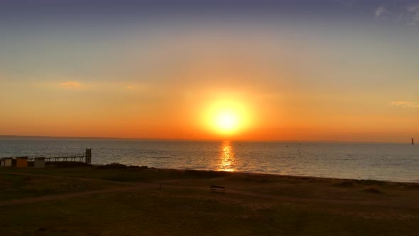 Bright red sunset at the beach with a park bench