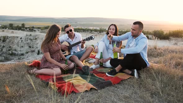 Four Cheerful People Open the Bottle and Cheering with Beer at Picnic