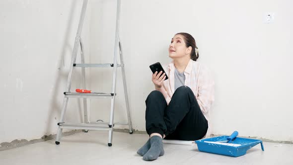 Young Woman with Black Hair Sits Near White Wall at Ladder