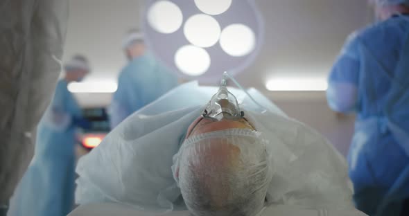 Patient with Anesthesia Mask Lying on Operating Table with Doctors Preparing for Surgery