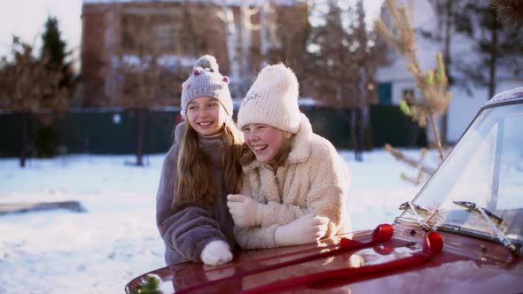 Portrait Two Laughing Teen Girl on Car Hood on Winter Landscape Background. Happy Young Girl in